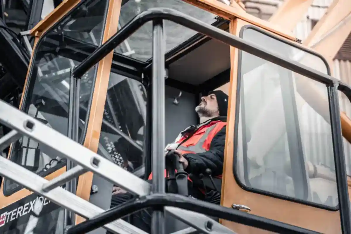 Machinist met reflecterende kleding zit in de cabine van een kraan.