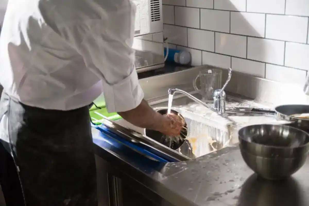 Keukenmedewerker wast keukengerei in een roestvrijstalen spoelbak.