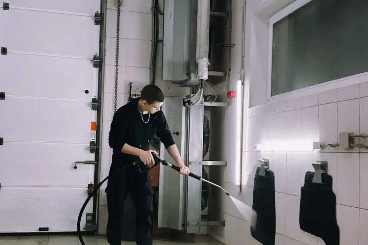 Medewerker reinigt een betegelde werkruimte met een hogedrukspuit.
