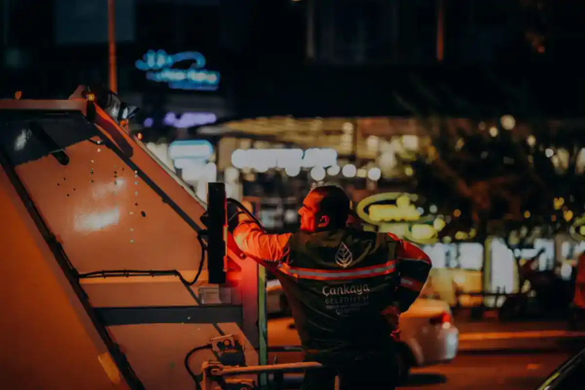 Afvalmedewerker staat bij een vuilniswagen tijdens avondwerk.