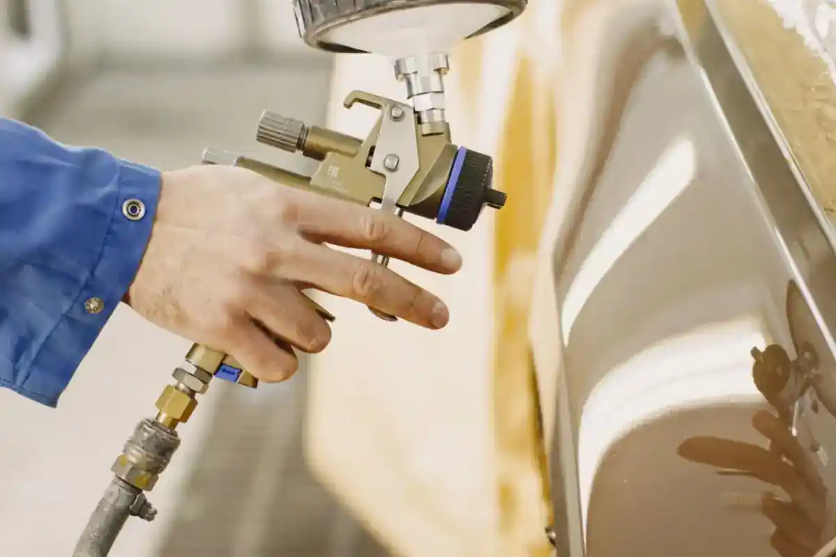 Hand met een verfspuit bij een carrosseriepaneel.