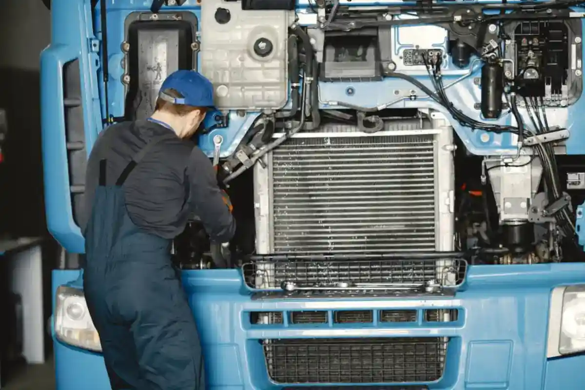 Monteur werkt onder het geopende voorpaneel van een blauwe vrachtwagen.