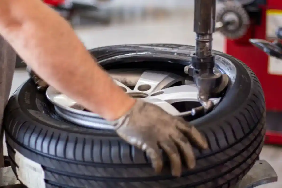Gehandschoende handen werken aan een autoband op een bandenmachine.
