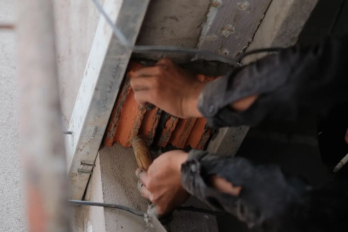 Handen bewerken met handgereedschap het metselwerk rond een opening.