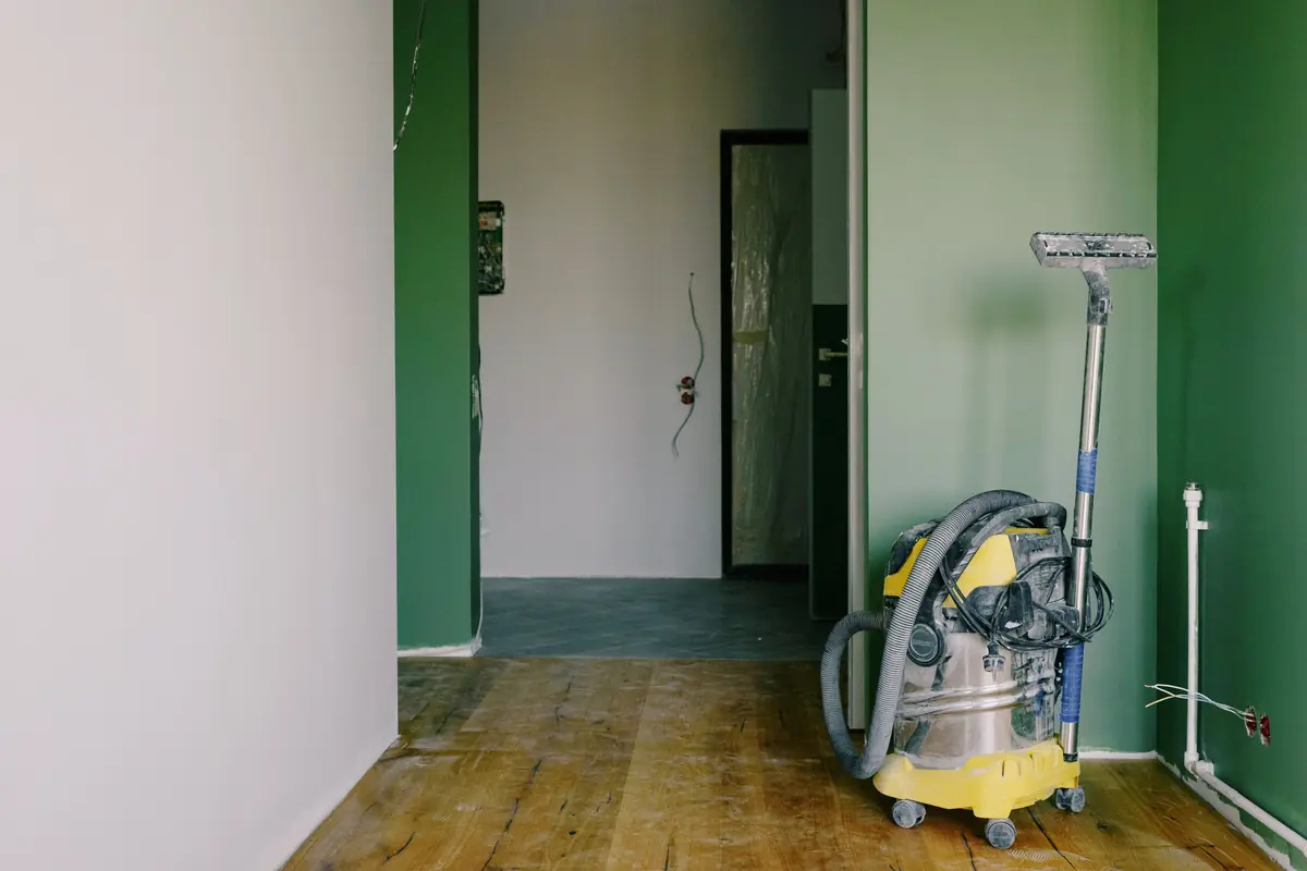 Een bouwstofzuiger staat op een houten vloer in een woning tijdens renovatie.