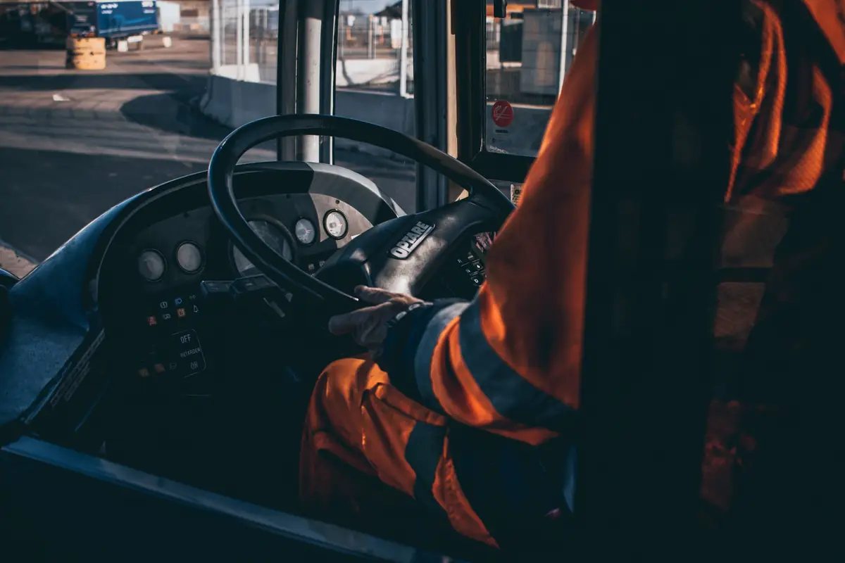 Een buschauffeur zit achter het stuur bij het dashboard van de bus.