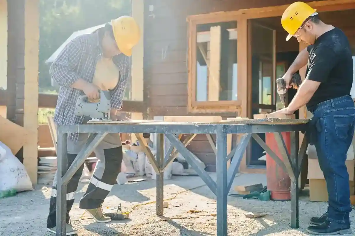 Twee timmerlieden werken met elektrisch gereedschap aan houten balken.