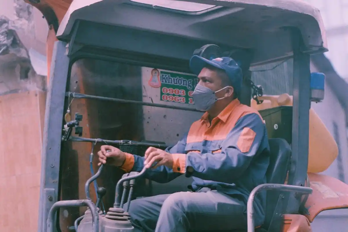 Machinist met helm zit aan de bedieningshendels van een graafmachine.