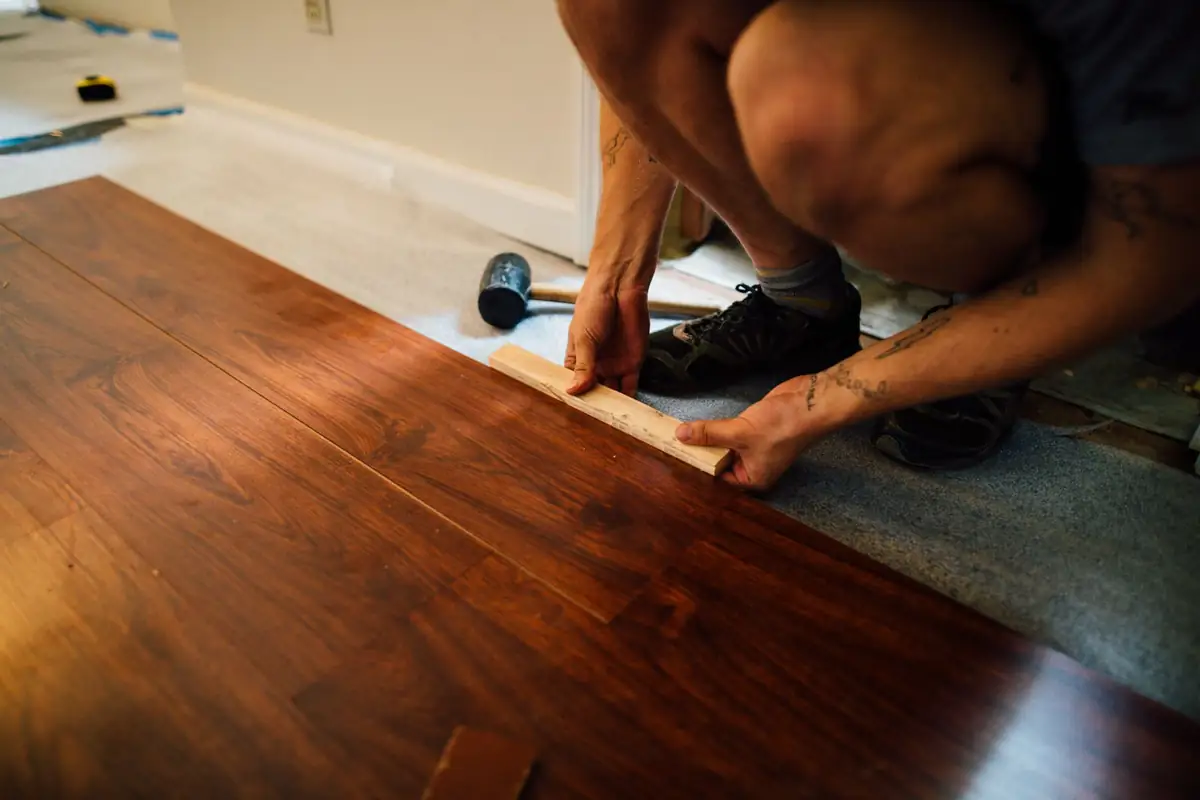 Medewerker legt houten vloerplanken met een slagblok en rubberen hamer.