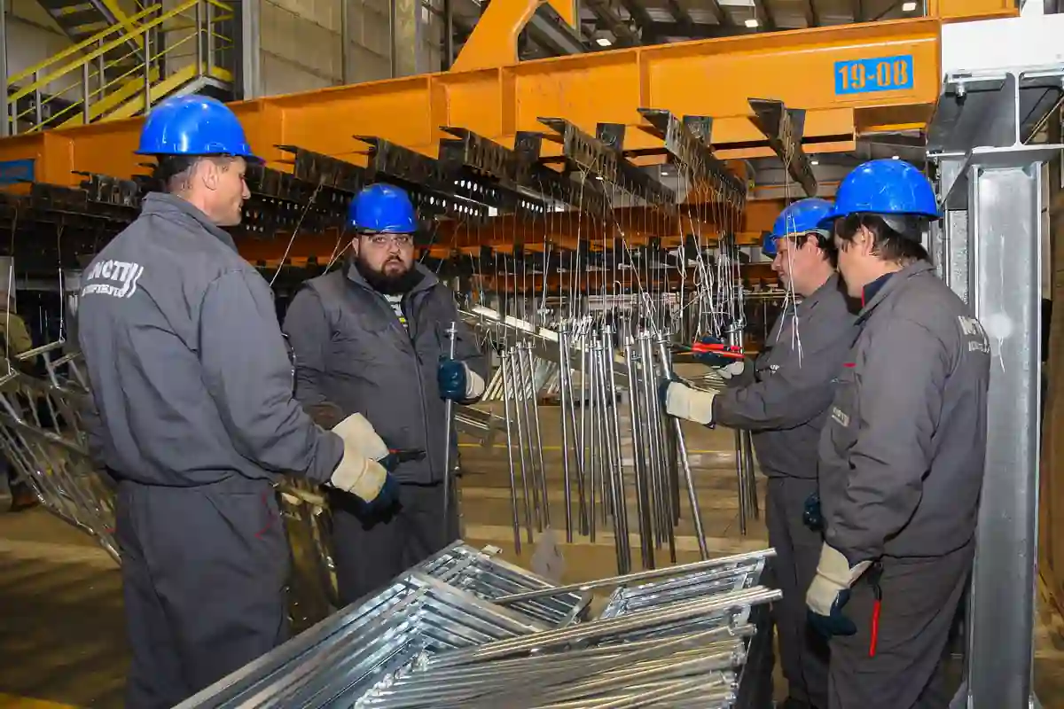 Medewerkers met helmen staan bij verzinkte metalen onderdelen aan een productielijn.