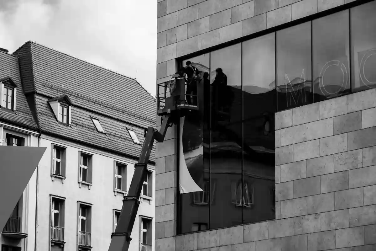 Zwart-witfoto van monteurs in een hoogwerker bij een glazen gevel.