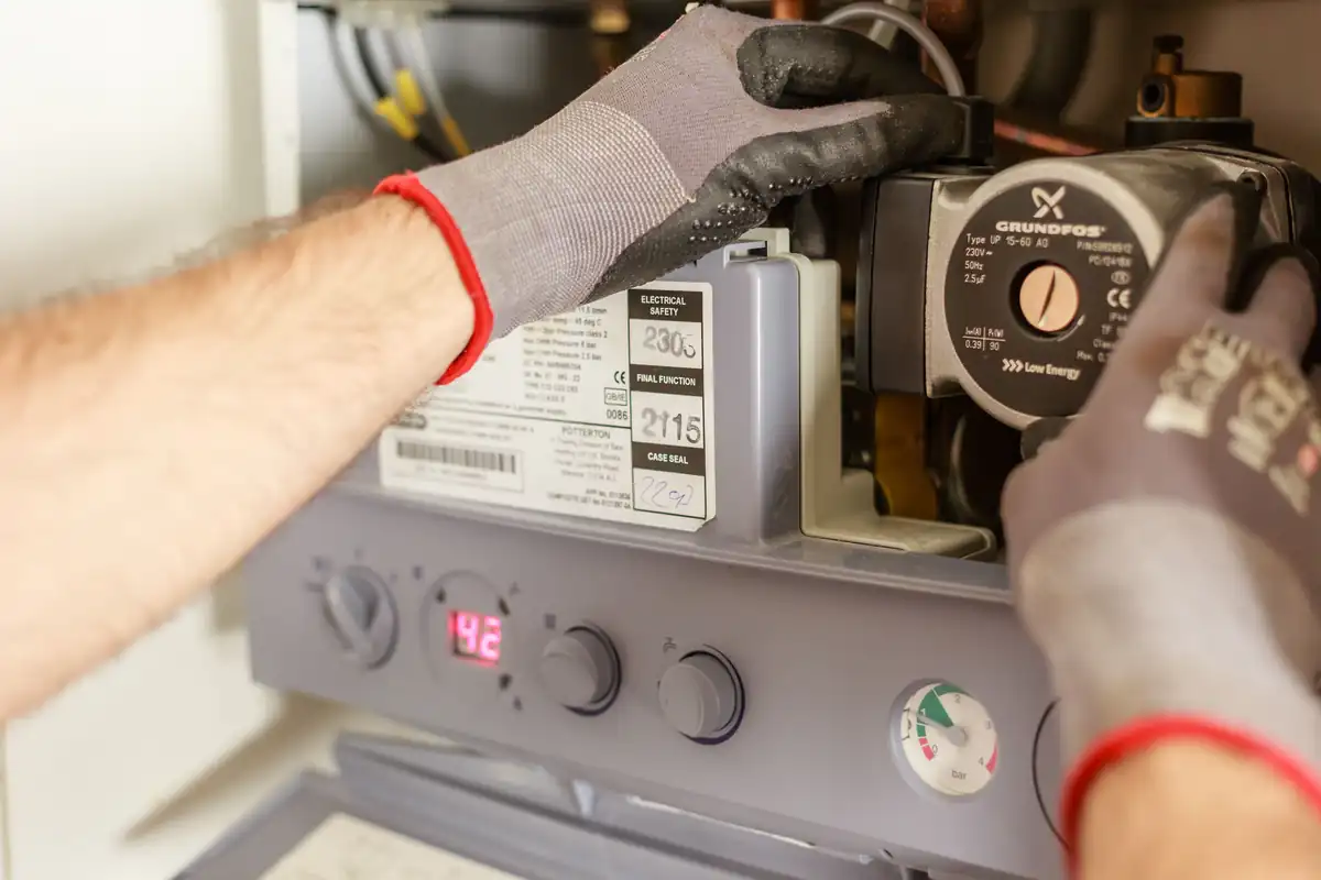 Gehandschoende handen werken aan de circulatiepomp in een verwarmingsketel.