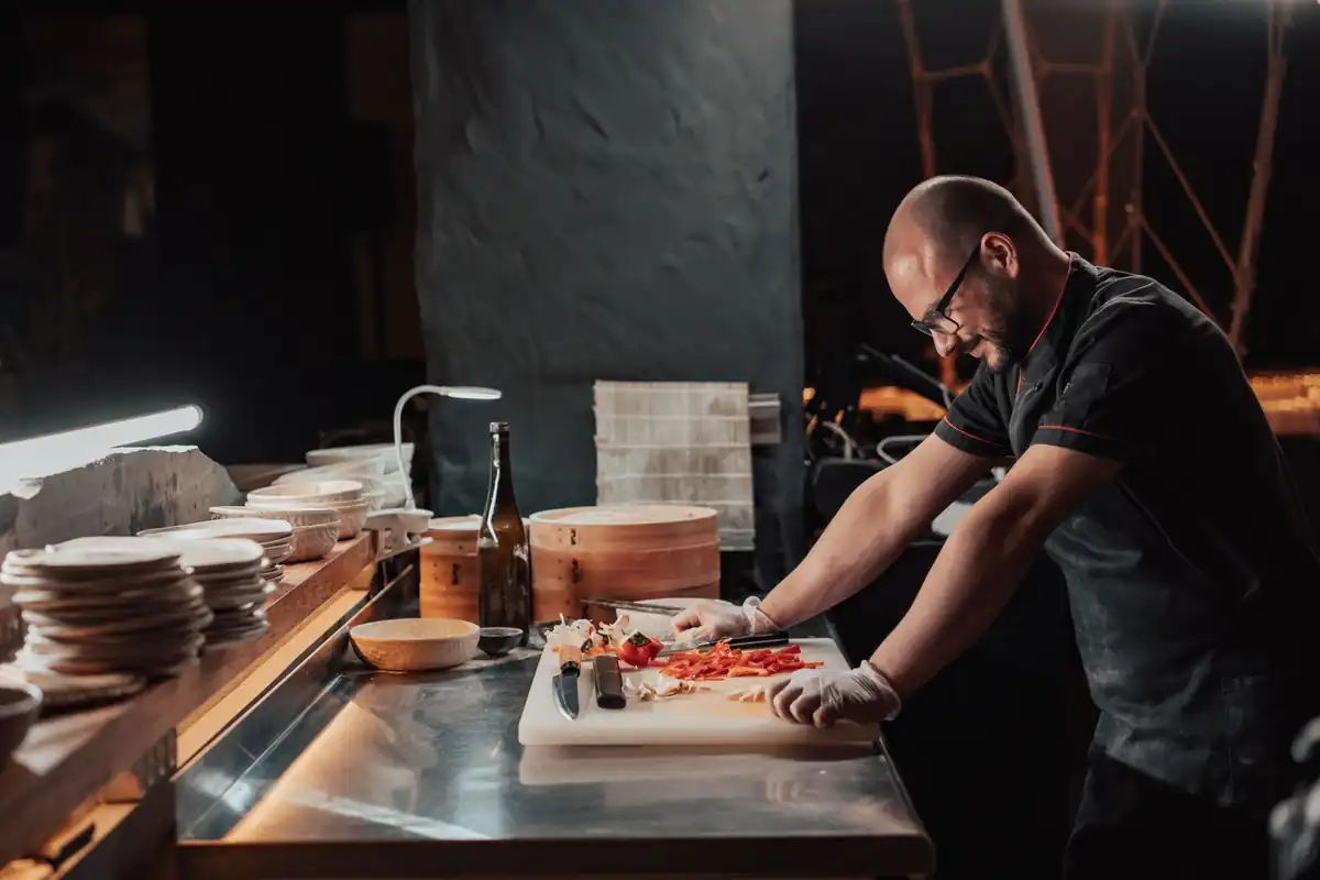 Keukenmedewerker snijdt groenten aan een werkblad in een restaurantkeuken.