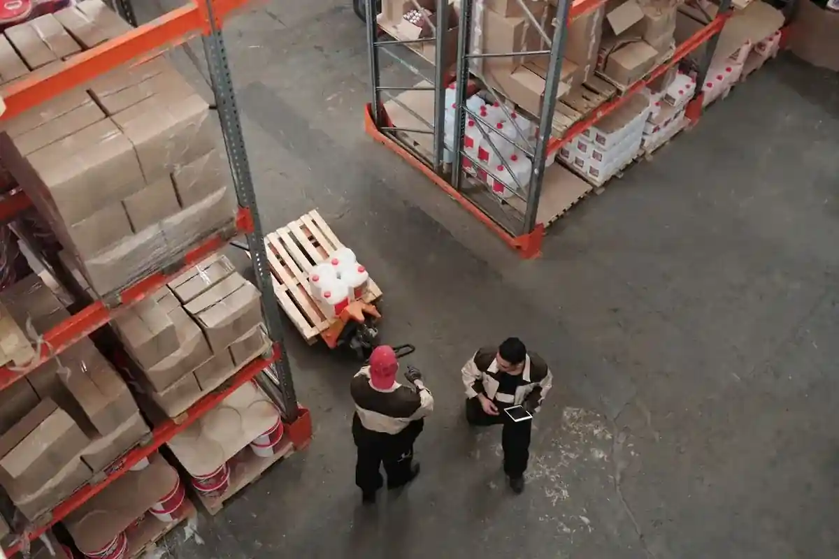 Twee magazijnmedewerkers tussen stellingen en pallets met goederen.