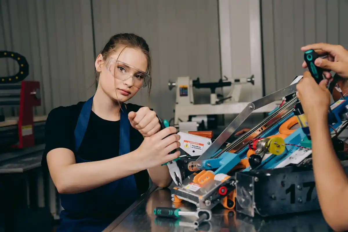 Medewerker met veiligheidsbril monteert een mechanisme aan een werkbank.