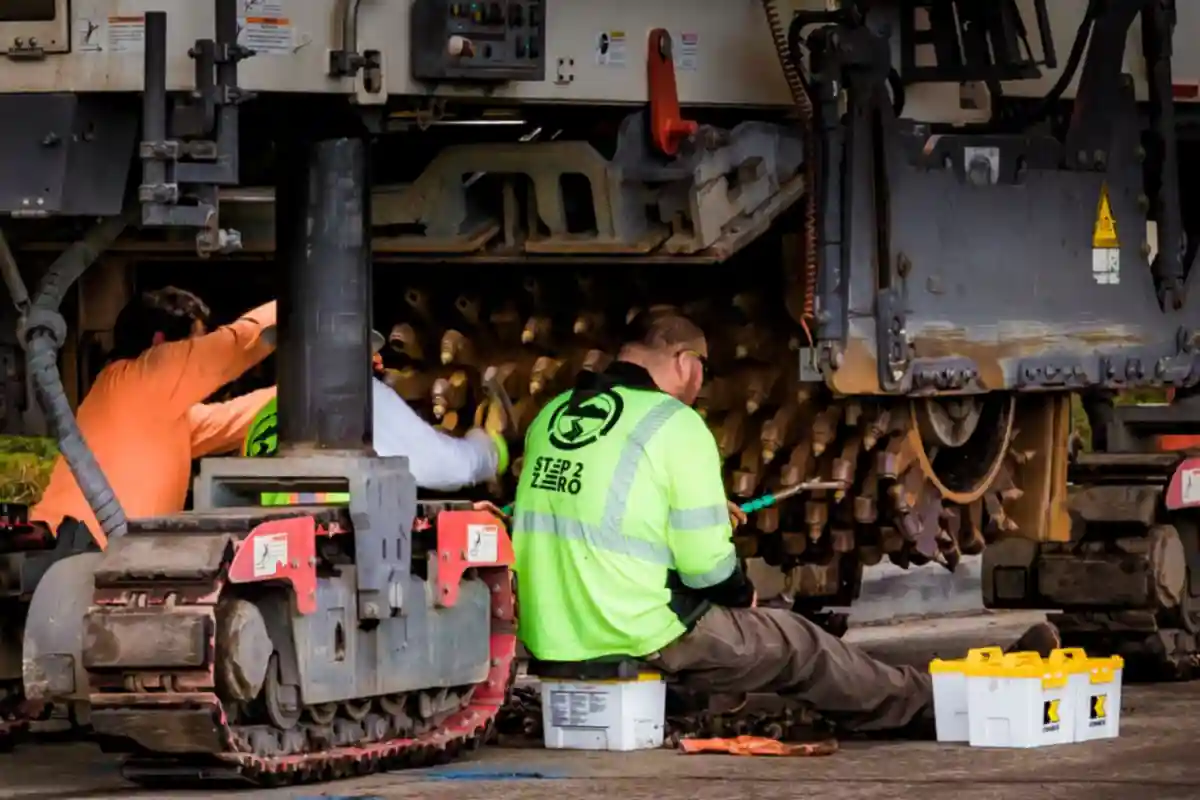 Monteurs werken aan het onderstel van een grote bouwmachine.