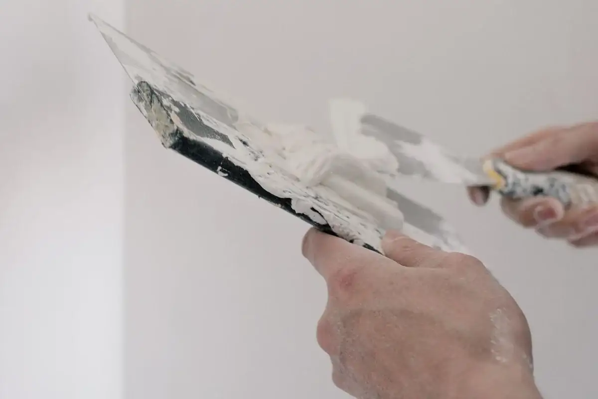 Handen werken met plamuurmessen aan de afwerking van een binnenmuur.