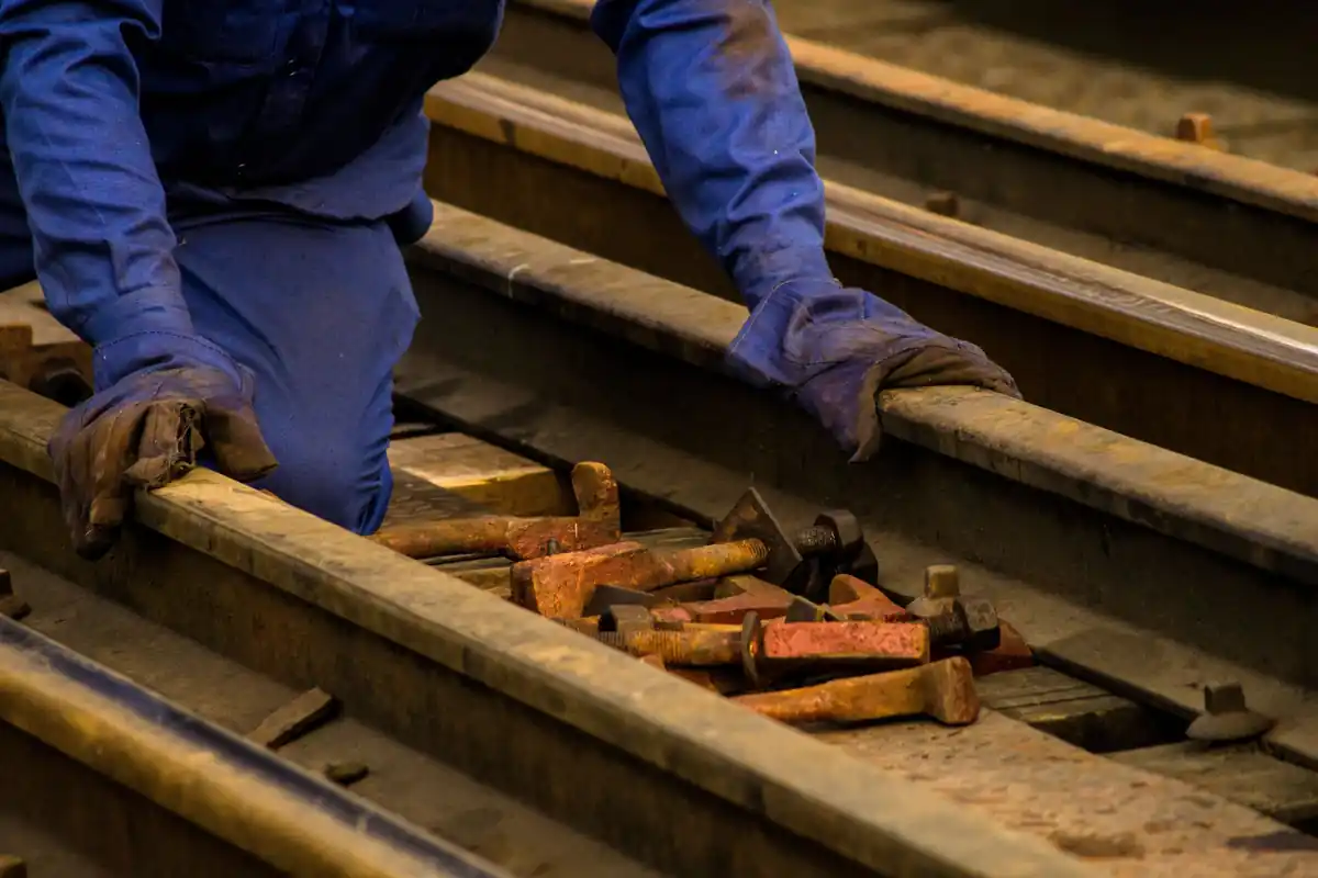 Gehandschoende handen van een spoorwerker bij rails en handgereedschap.