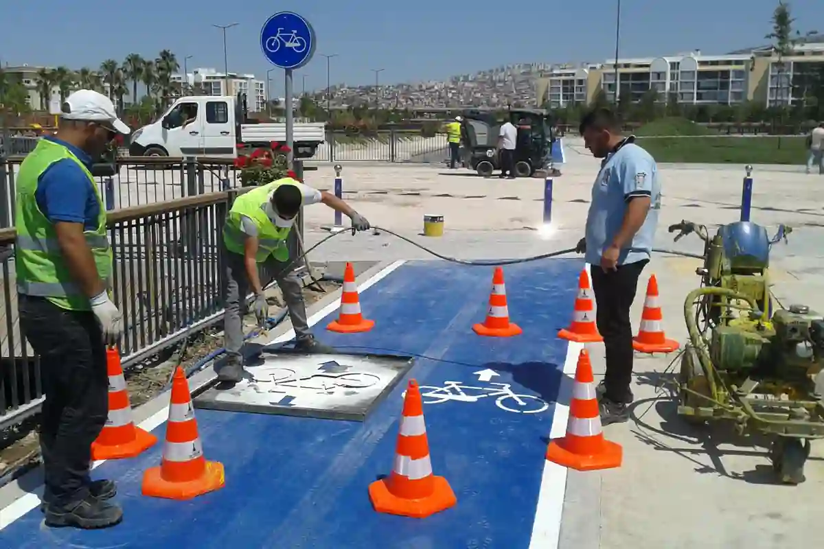 Medewerkers brengen met een sjabloon een witte fietsmarkering aan op een blauw fietspad.