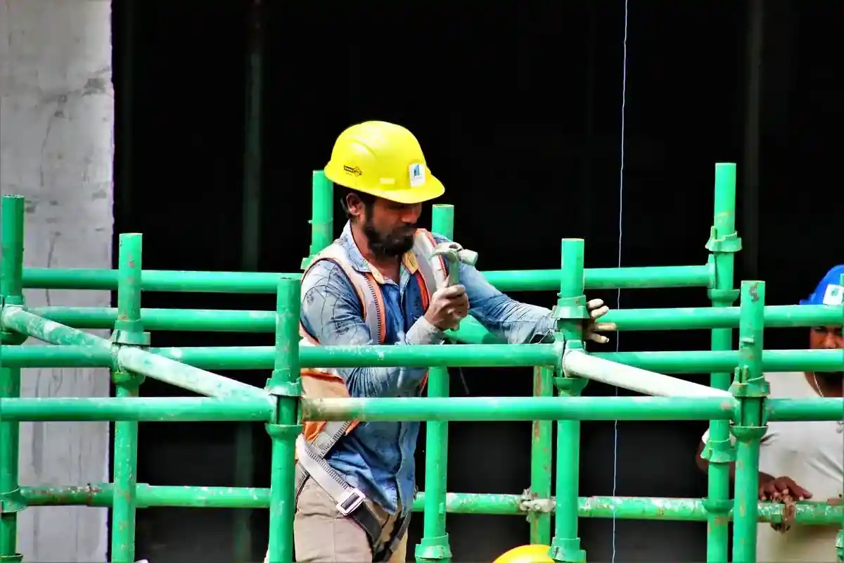 Steigerbouwer met helm en harnas werkt aan een steigerconstructie.