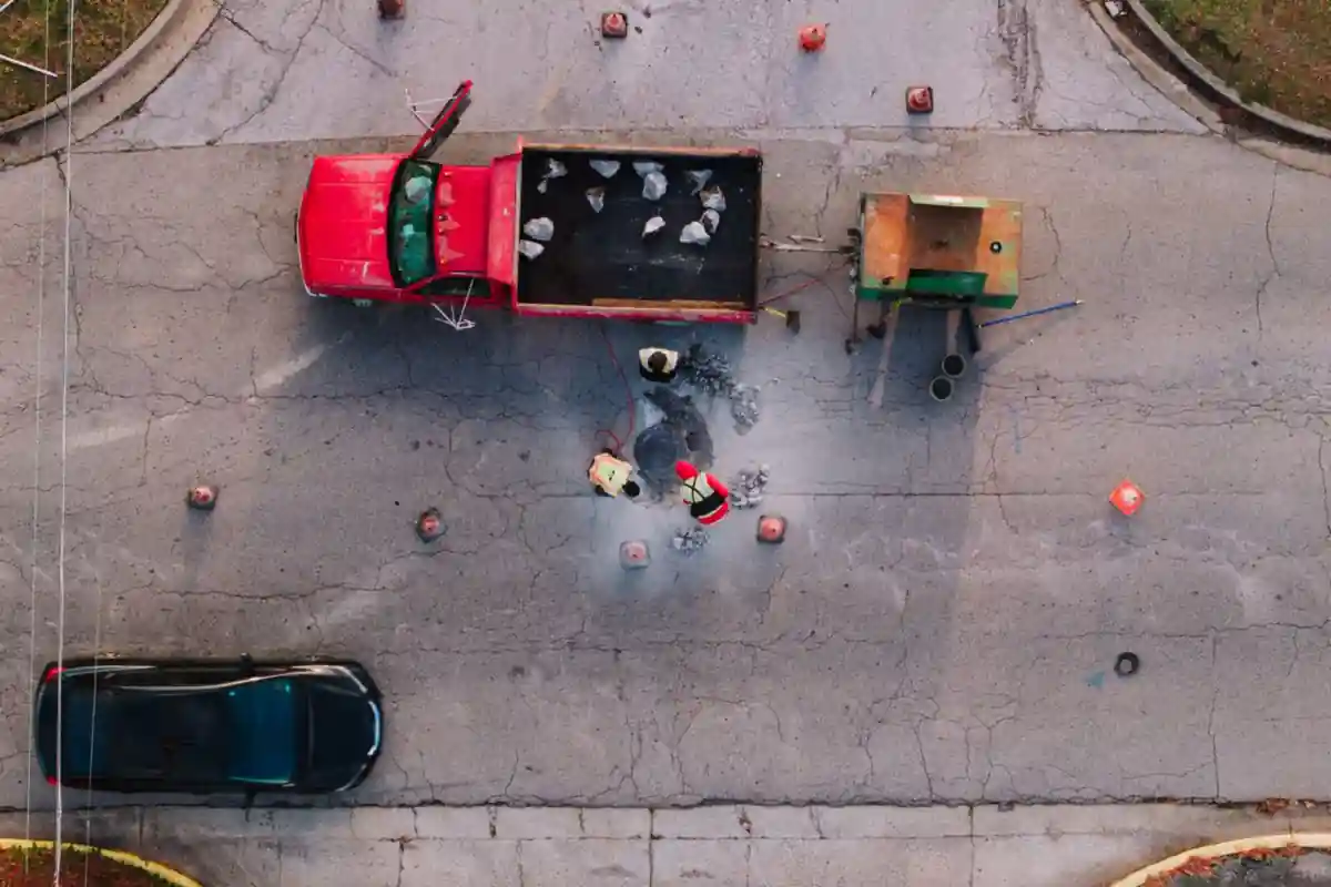 Bovenaanzicht van medewerkers en materieel rond een put in een straat.