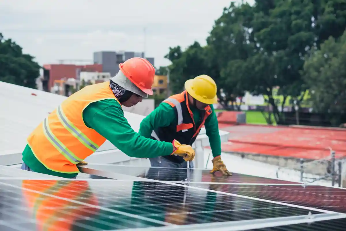 Twee monteurs met helmen en veiligheidshesjes werken aan zonnepanelen op een dak.