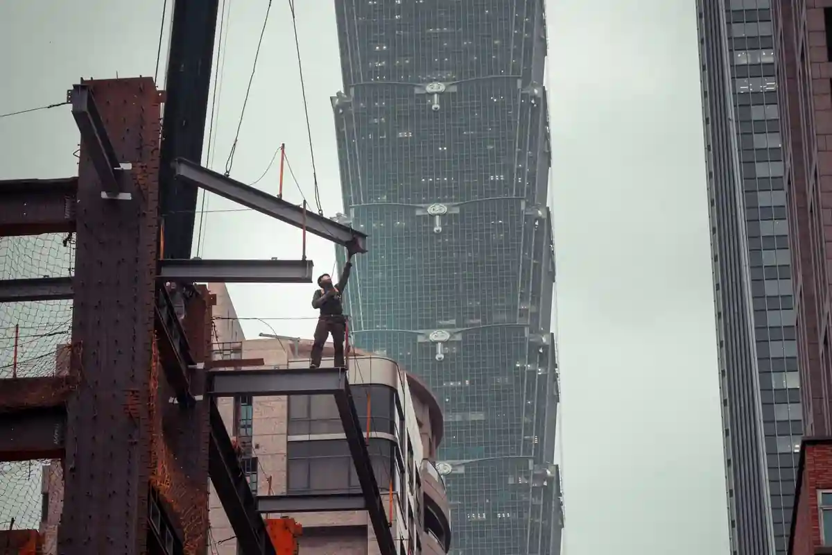 Bouwmedewerker staat op stalen balken van een gebouw in aanbouw.