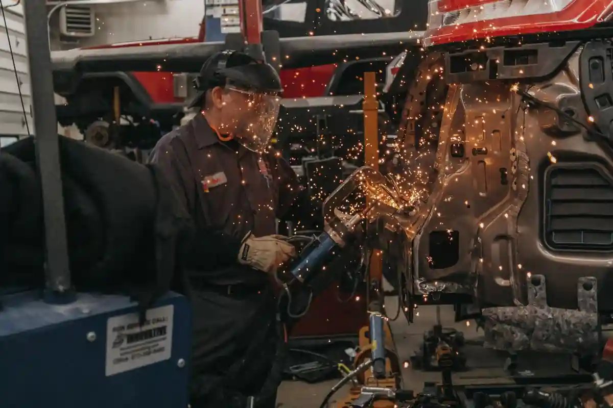 Vakman met gelaatsbescherming werkt aan de metalen carrosserie van een voertuig.