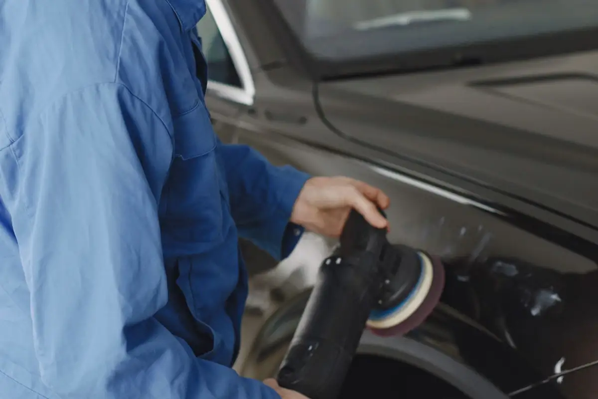 Medewerker bewerkt een carrosseriepaneel met een elektrische polijstmachine.