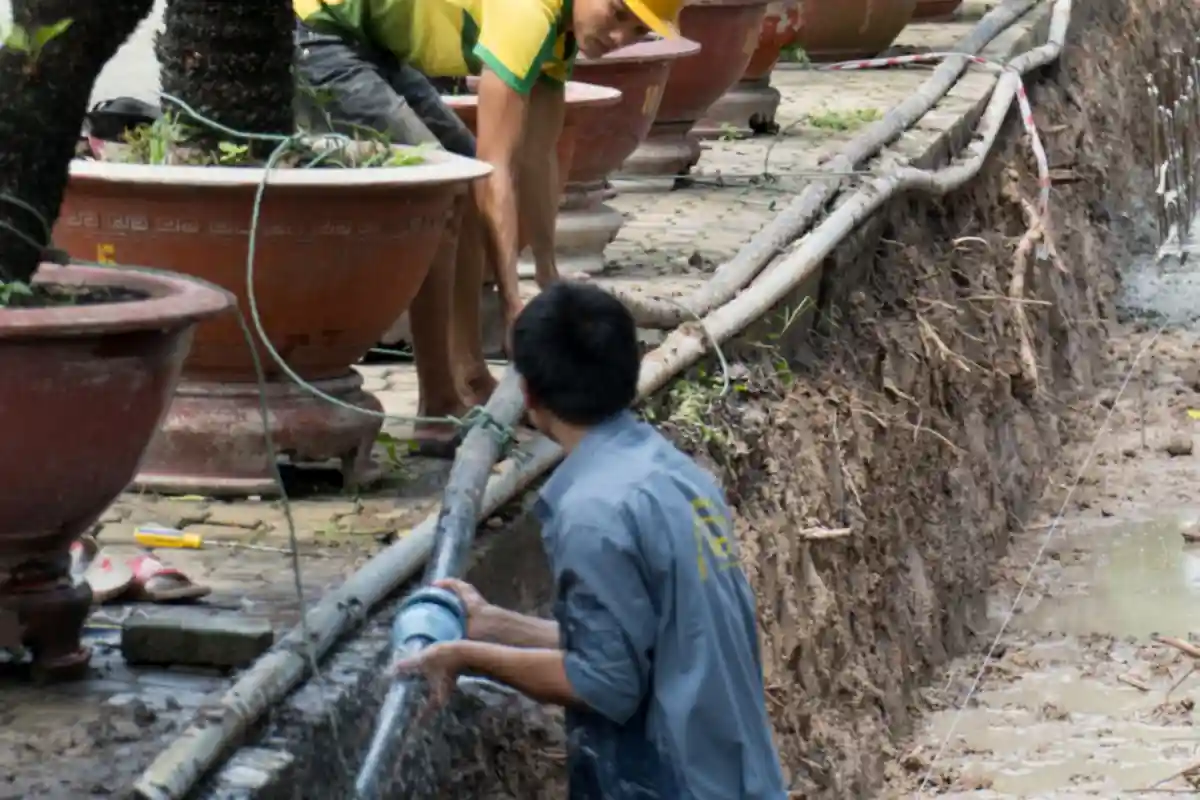 Medewerker werkt aan een waterleiding in een uitgegraven sleuf.